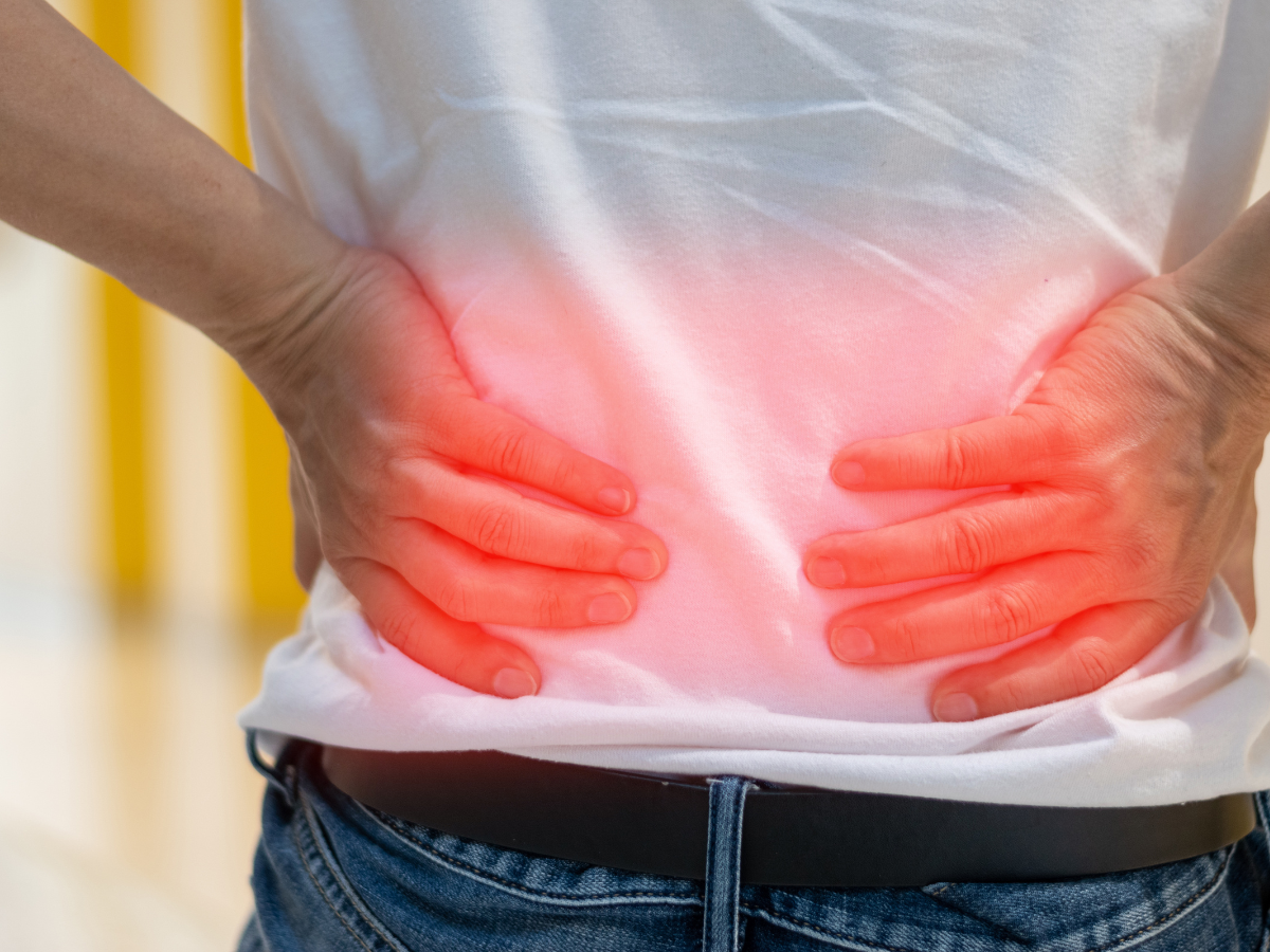Person holding lower back, indicating pain with red glow; wearing jeans and white shirt.