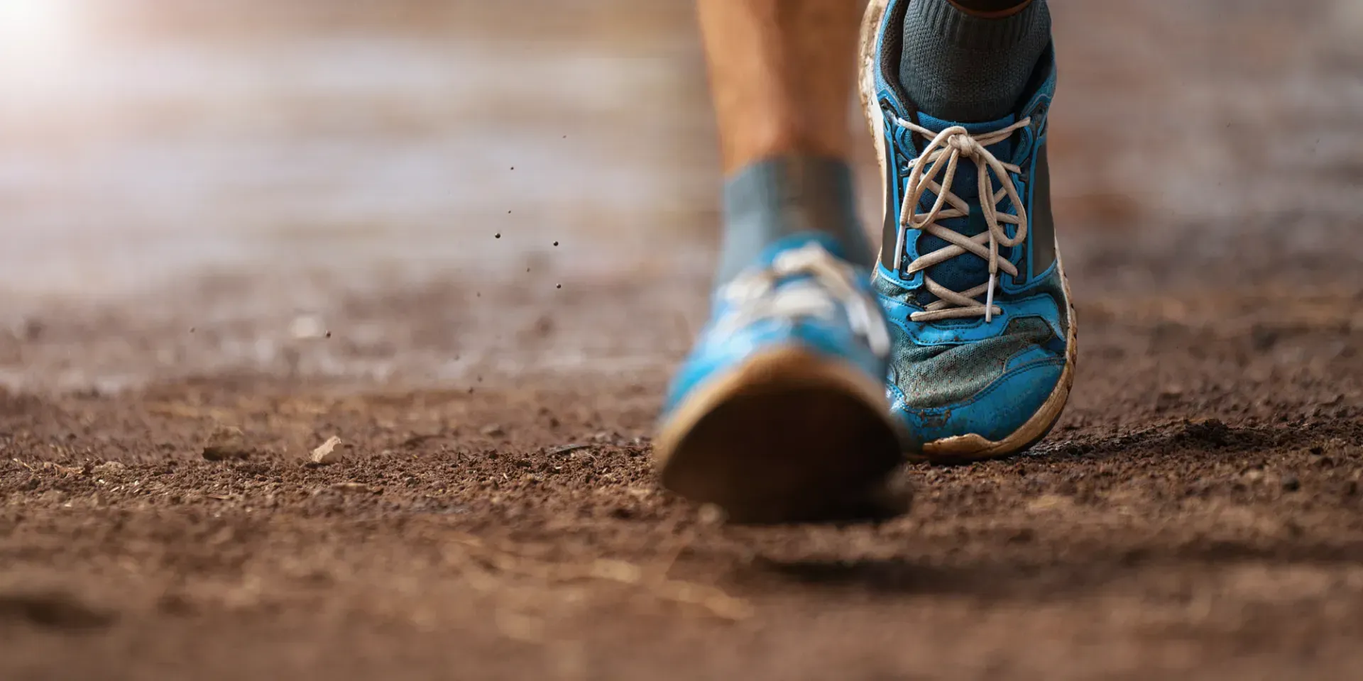 A person wearing blue running shoes is walking on a dirt road.