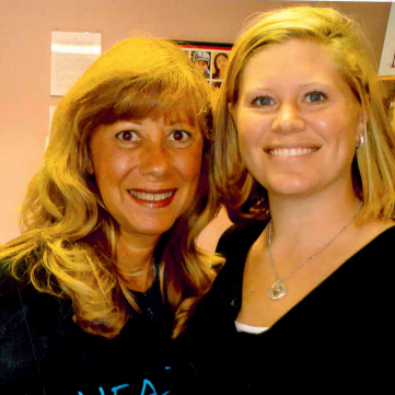 Two women are posing for a picture and one of them is wearing a black shirt with the letter a on it