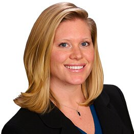 A woman wearing a black jacket and a blue shirt smiles for the camera