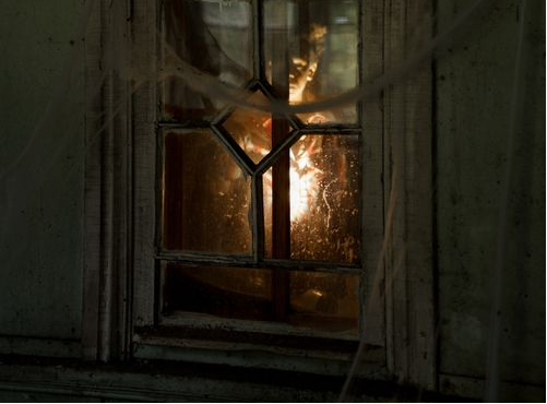 An image shows a glowing light illuminating the window of an abandoned building.
