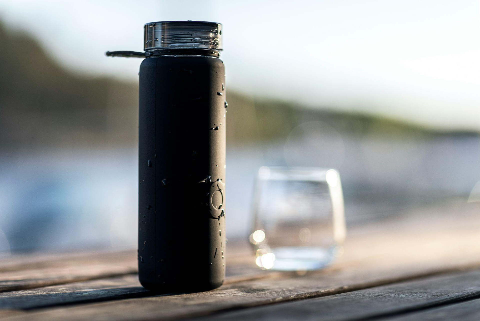 a black water and a glass on a wooden surface