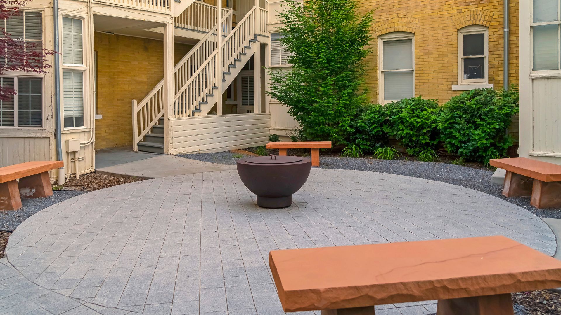There is a fire pit in the middle of the courtyard surrounded by benches. The patio is grey block paving in Essex