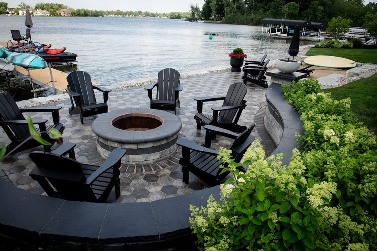 Fire pit with Adirondack chairs, near a lake.