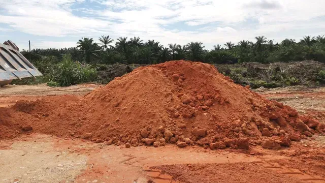 A large mound of reddish-brown earth or clay soil which is building materials piled up on a construction site.