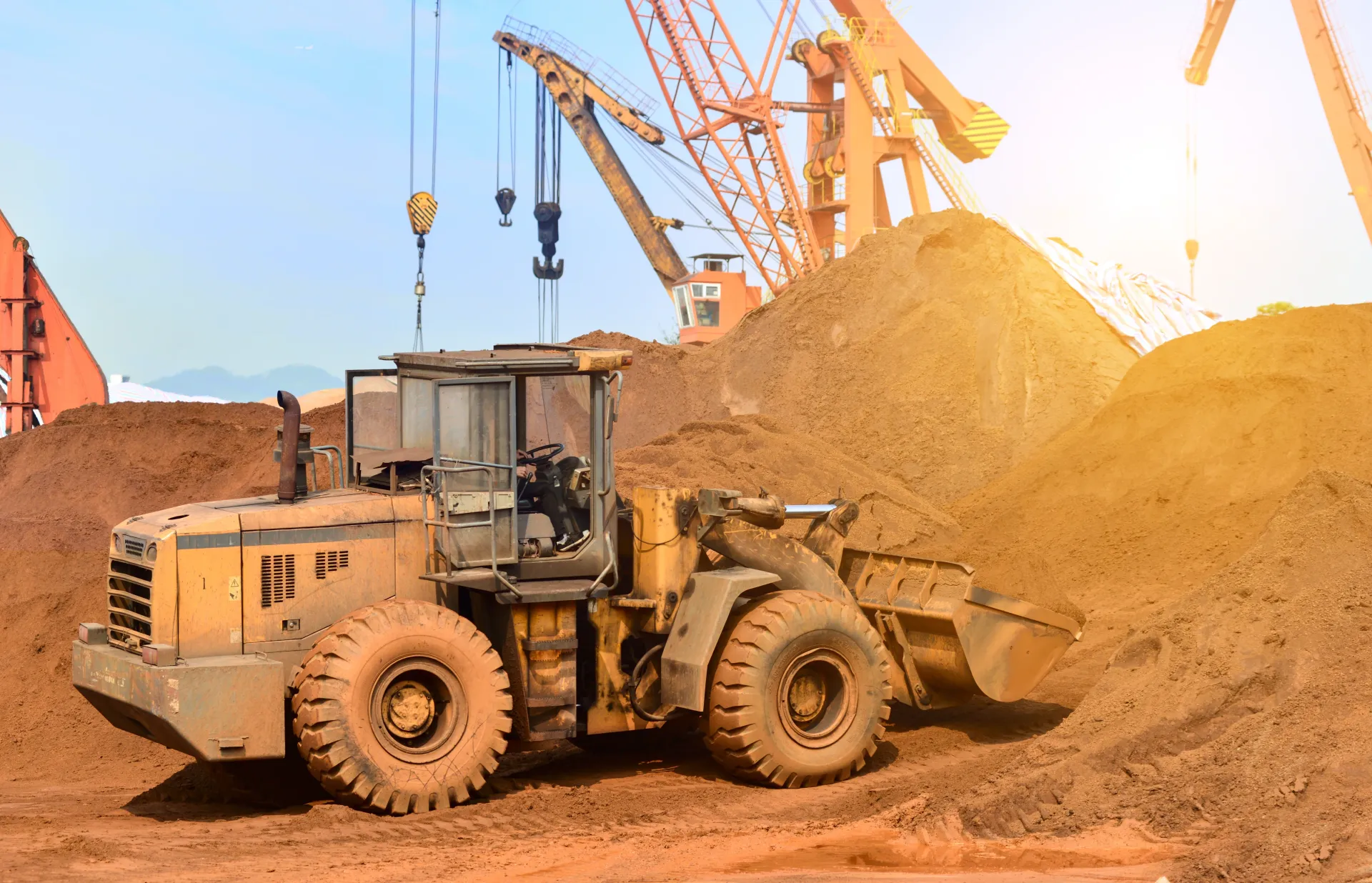 A construction site featuring a large yellow excavator in operation, scooping soil and debris in a sandpit.