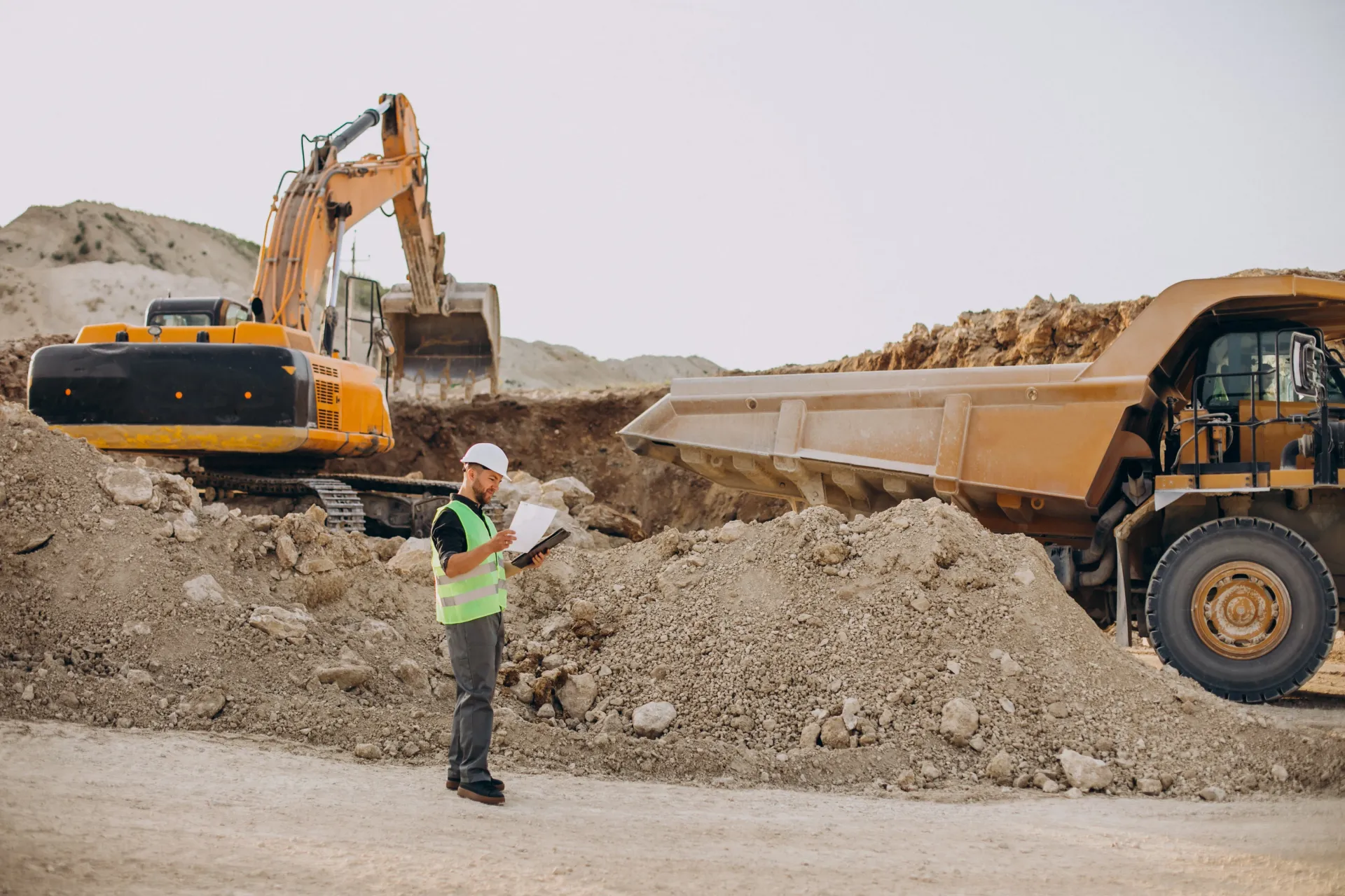 In a sandpit there is a planner looking carefully at the drawings in his hand so that the plan will be completed on time.