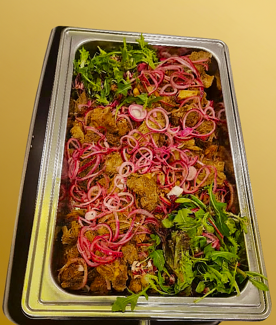 Bricka med kryddat kött med rödlöksskivor och grönbladig garnering.