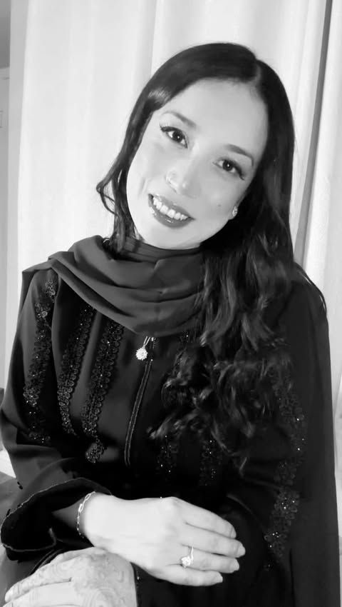 A woman is sitting at a desk with a laptop and a vase of flowers.