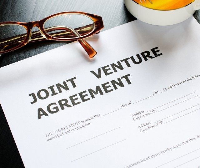 Joint Venture Agreement on a desk with glasses and a mug.