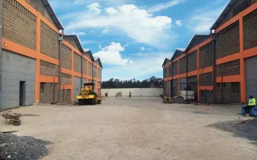 Two large industrial buildings, orange accents, outdoor area, construction equipment present, sunny day.