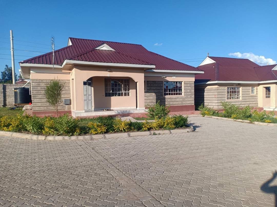 Houses with red roofs and stone walls, set on a cobblestone road, with greenery around.