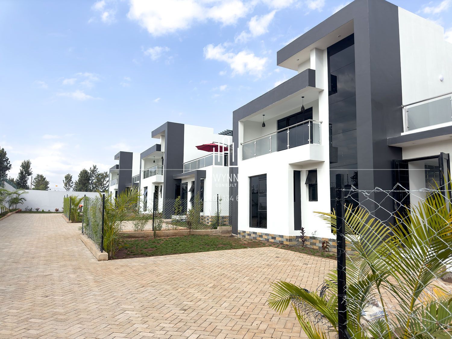 Modern townhouses with gray and white exteriors, a paved driveway, and green landscaping under a cloudy sky.