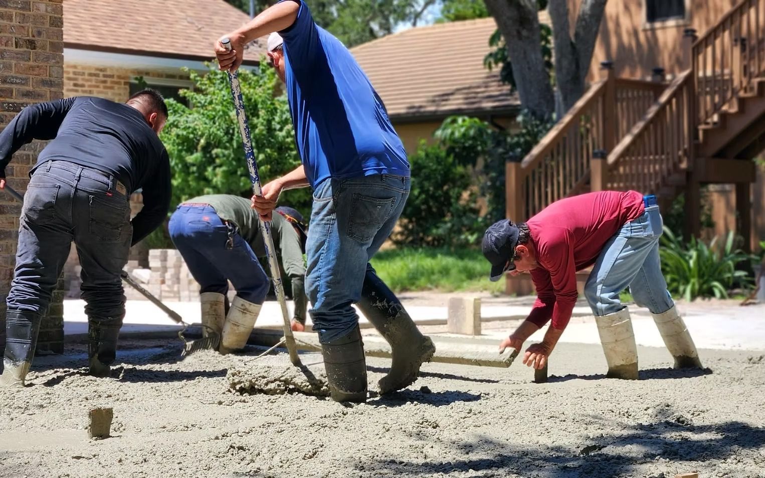 Construction workers spreading concrete with tools outdoors.