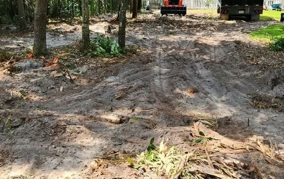 Dirt clearing with trees, tire tracks, and construction equipment in the background.