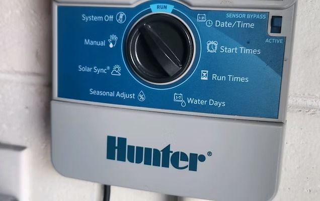 A blue and gray Hunter brand irrigation system control panel mounted on a brick wall.