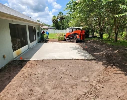 Concrete patio next to a house under construction; a skid steer is in the background.