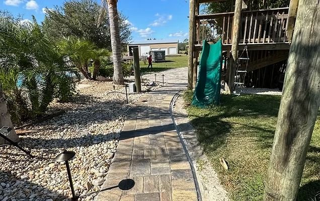 Brick pathway leading to a building, passing a play structure with a green slide and landscaping.