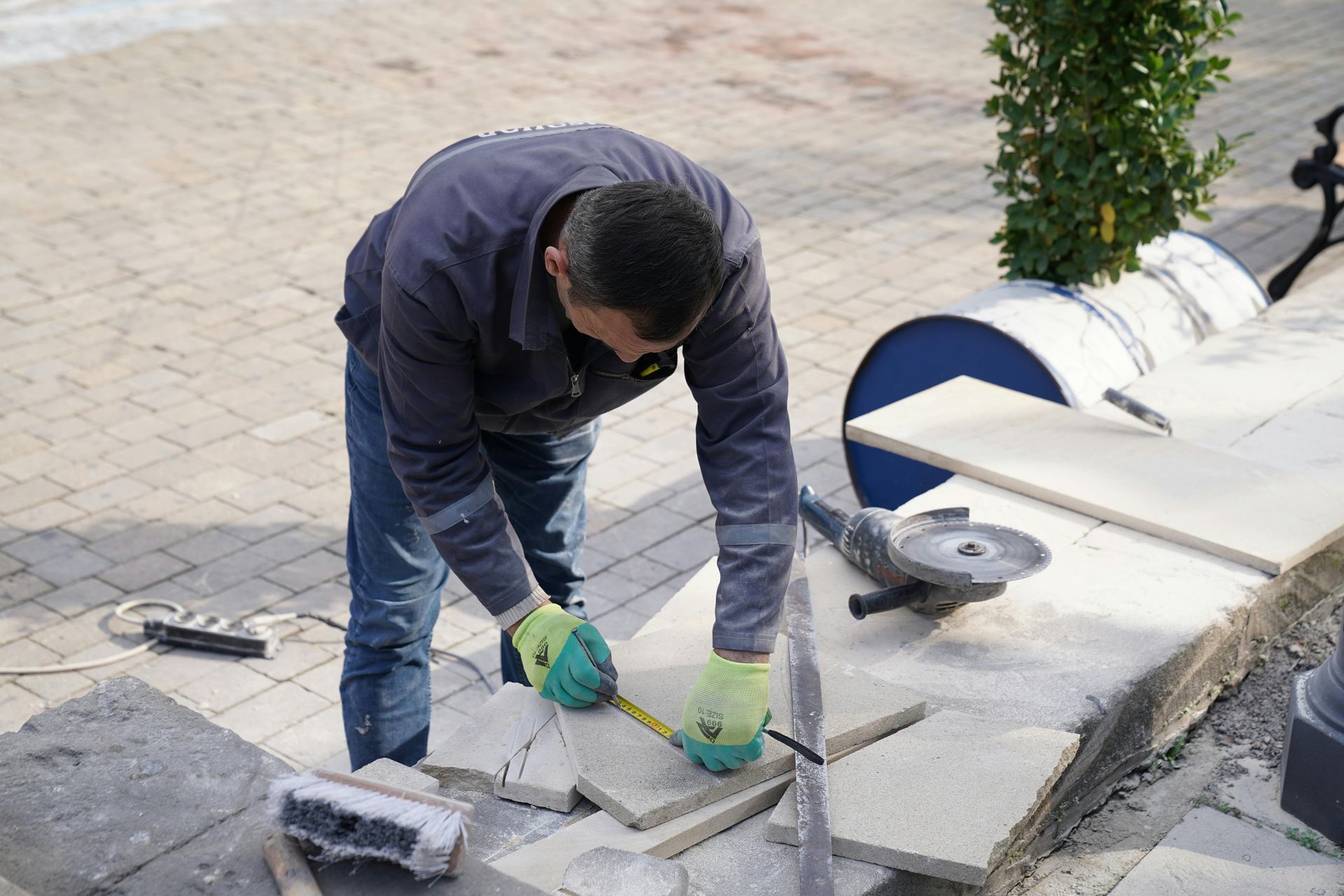 Worker in gloves cutting concrete pavers with a power saw outdoors