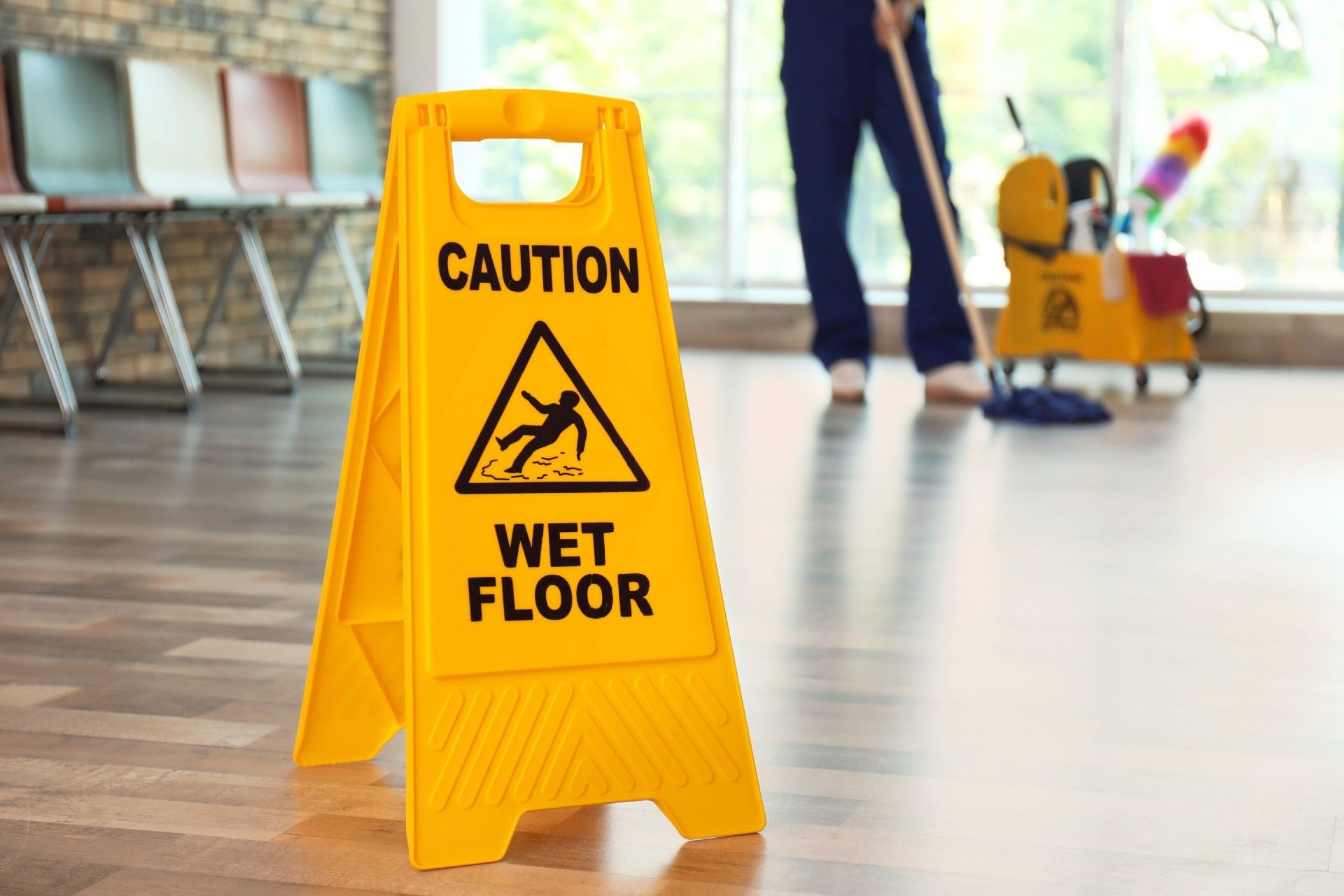A caution wet floor sign is on the floor in front of a man mopping the floor.