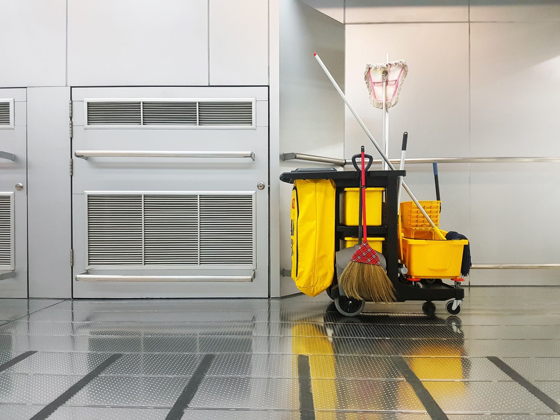 A cleaning cart with a mop , broom and bucket in a room.