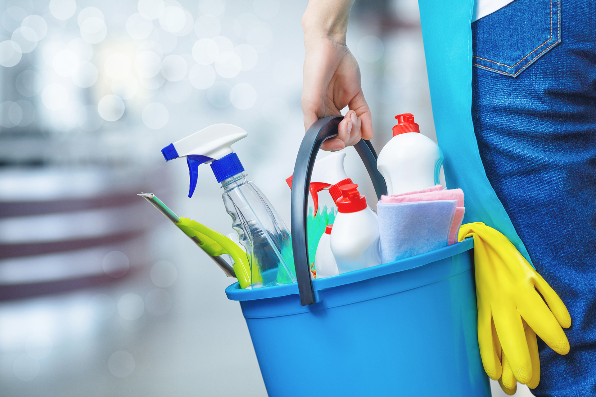 A woman is holding a blue bucket filled with cleaning supplies.
