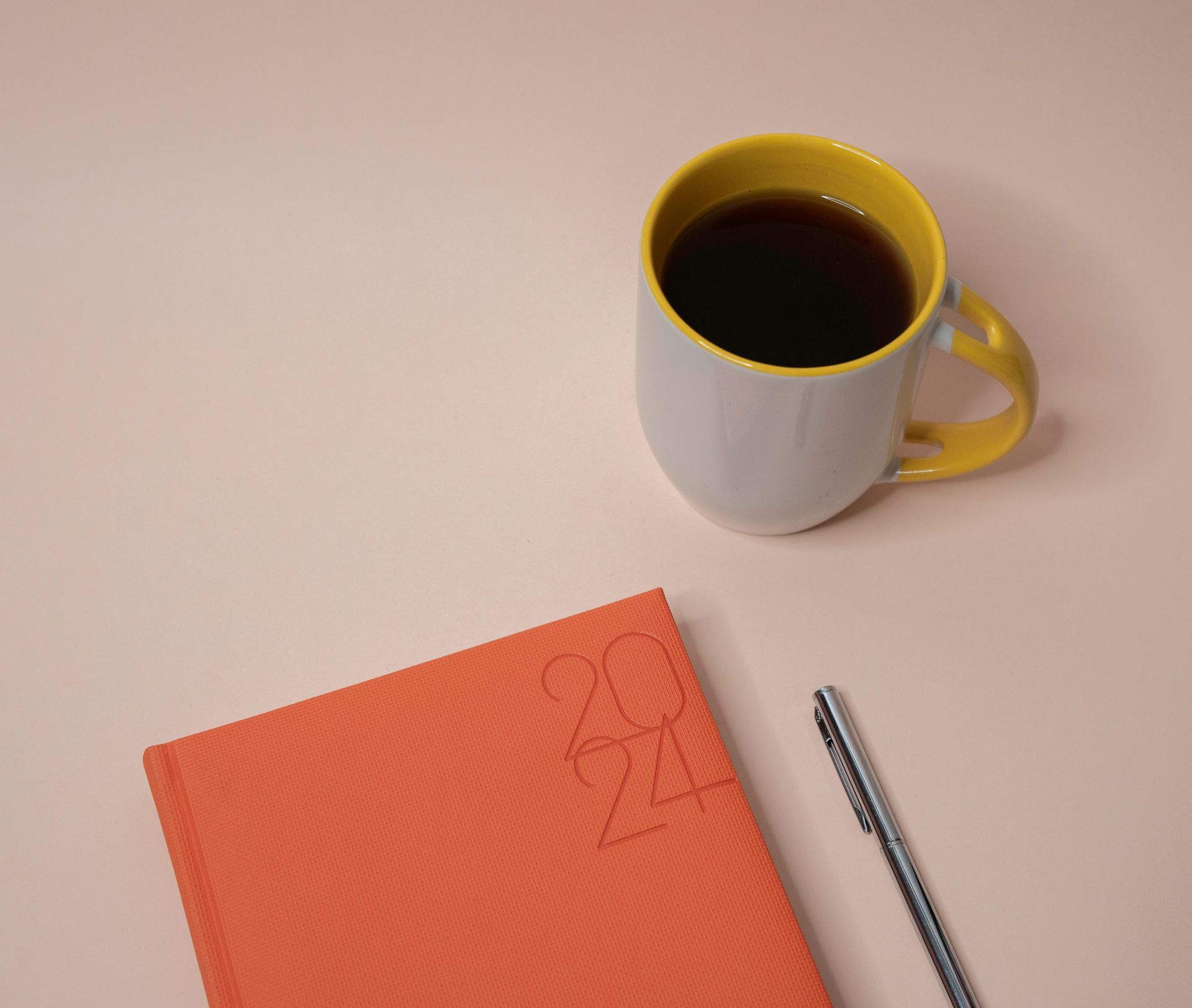 A cup of coffee sits next to a notebook and pen