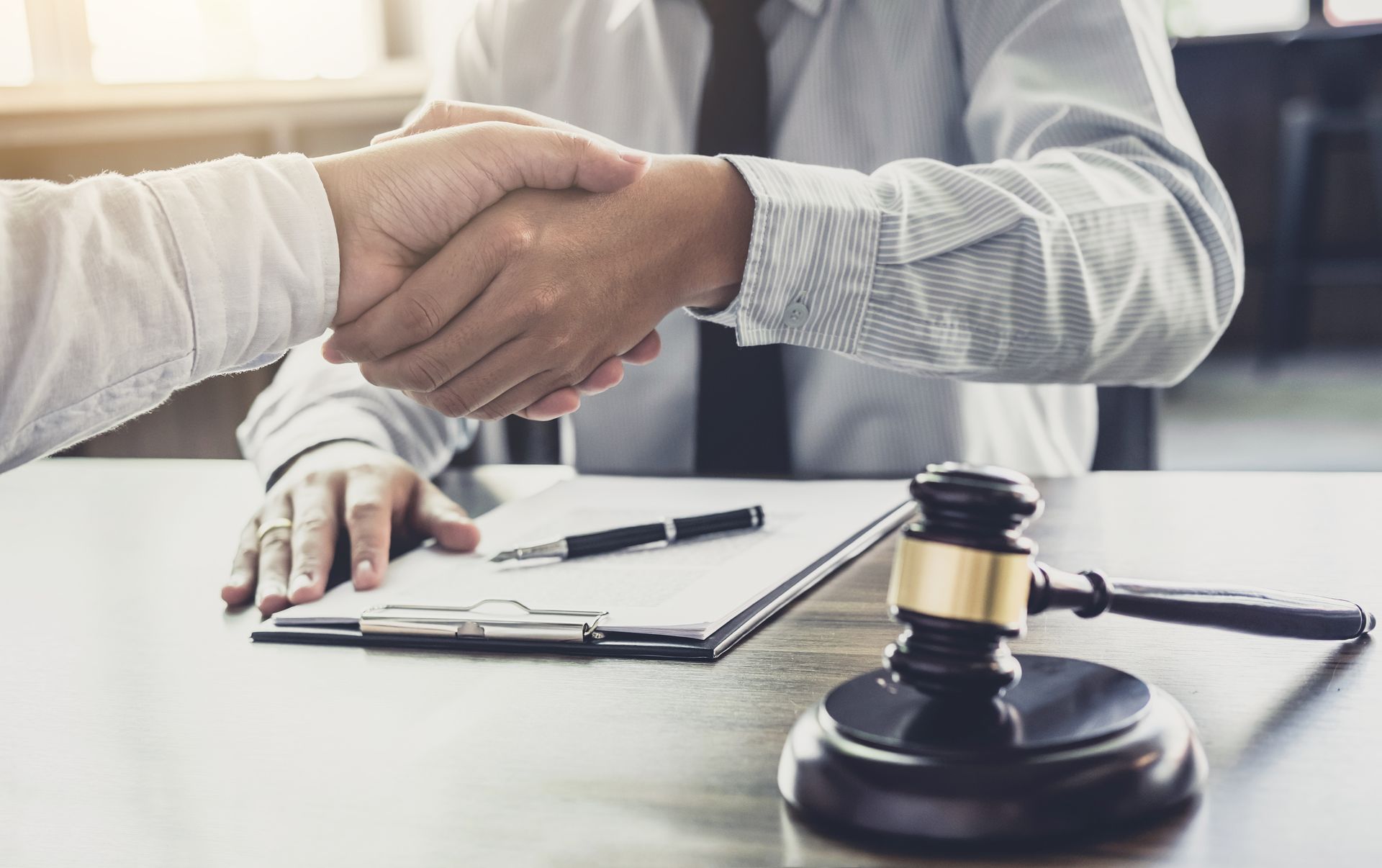 A man is shaking hands with another man while sitting at a table with a judge 's gavel.