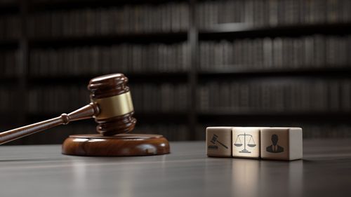 A wooden judge 's gavel and a wooden block with a scale of justice on it are on a table.