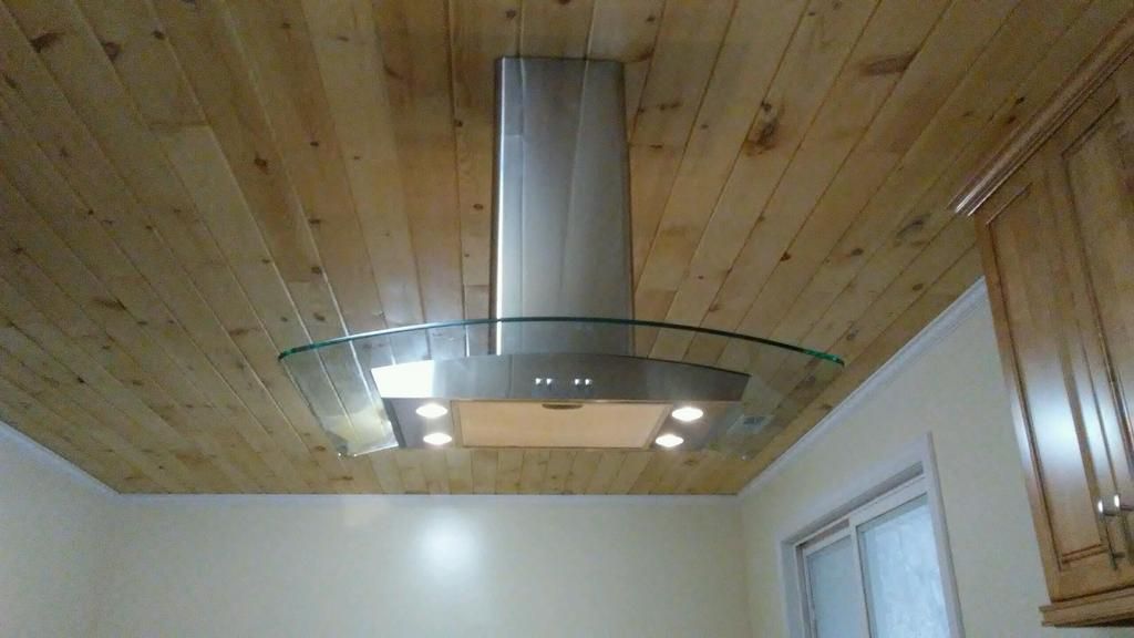A stainless steel hood is hanging from the ceiling of a kitchen.
