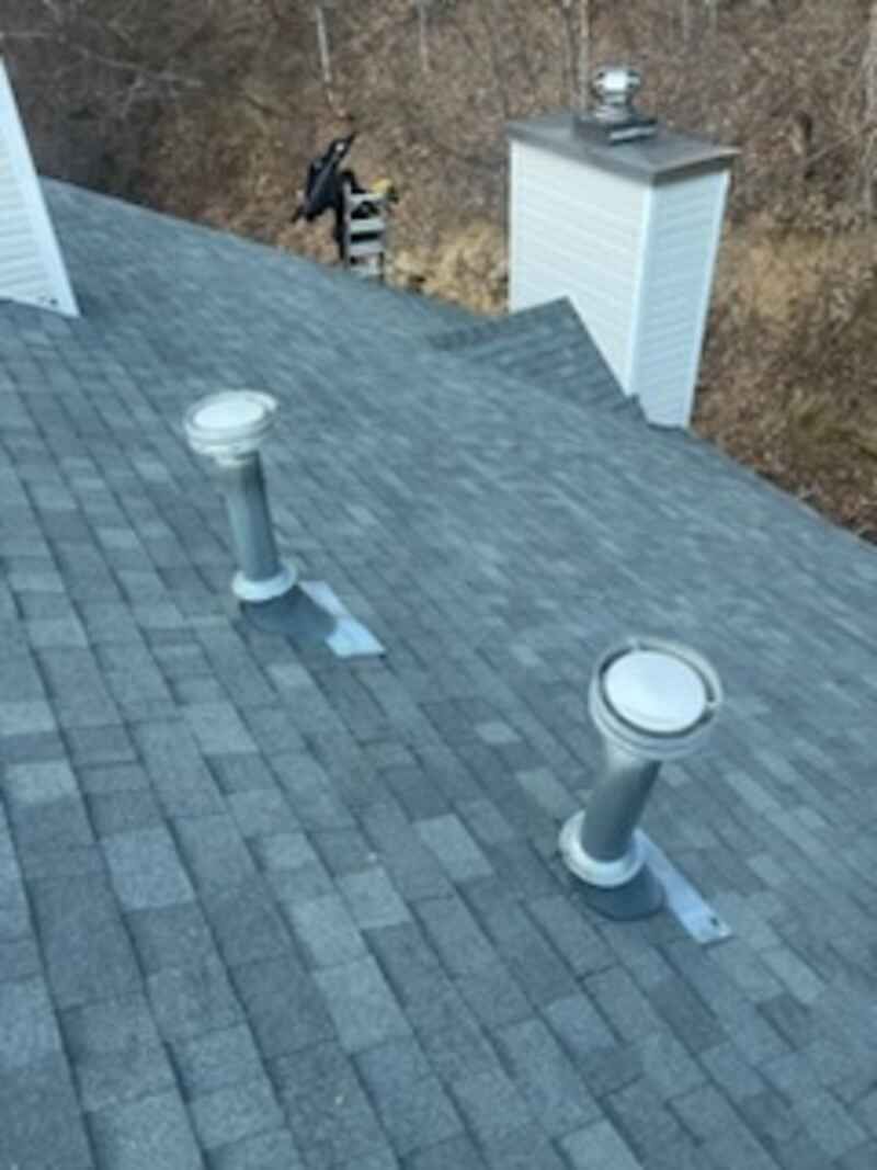 A roof with two chimneys and two skylights on it.