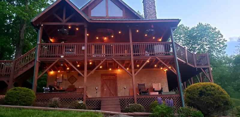 A large wooden house with a lot of windows and lights on the porch.