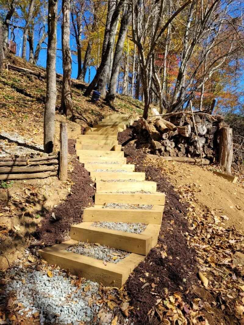 A set of wooden stairs leading up a hill in the woods.