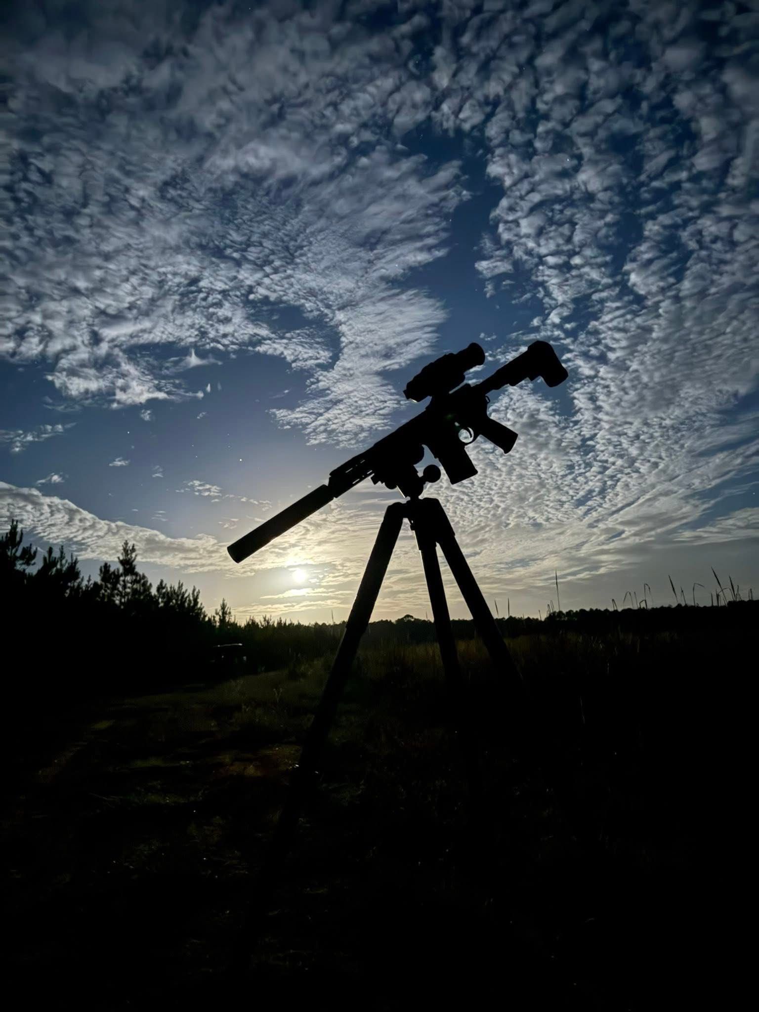Silhouette of a telescope on a tripod against a sunset sky with clouds.