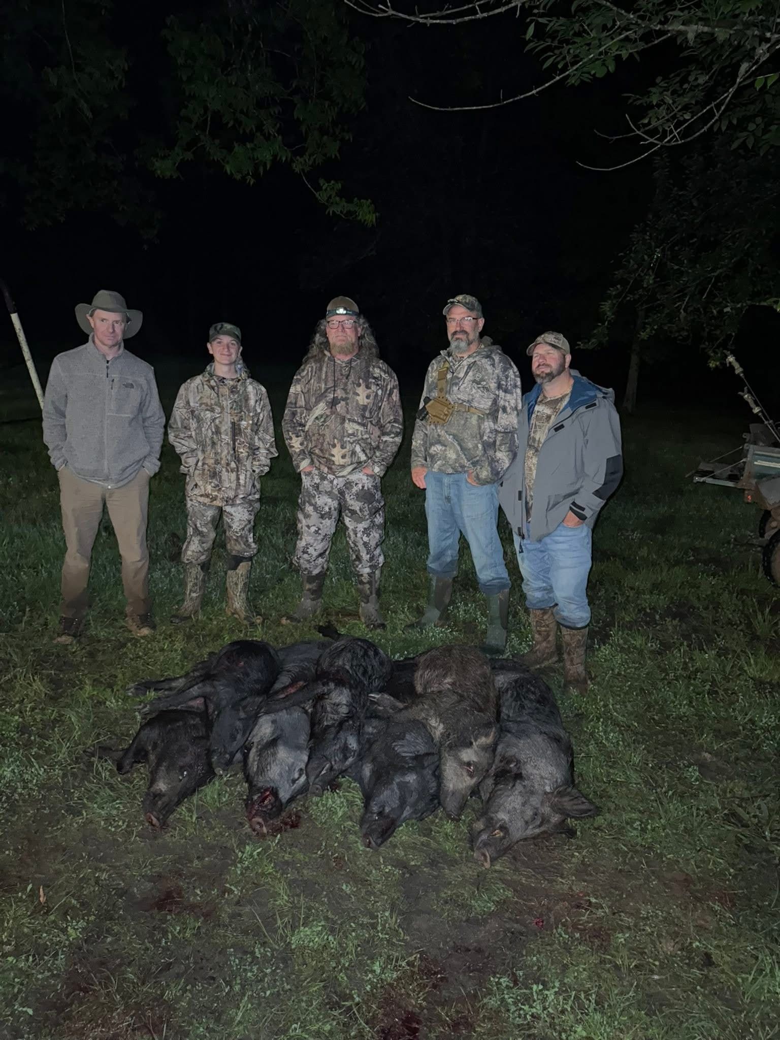 A group of hunters pose with several dead wild pigs at night.
