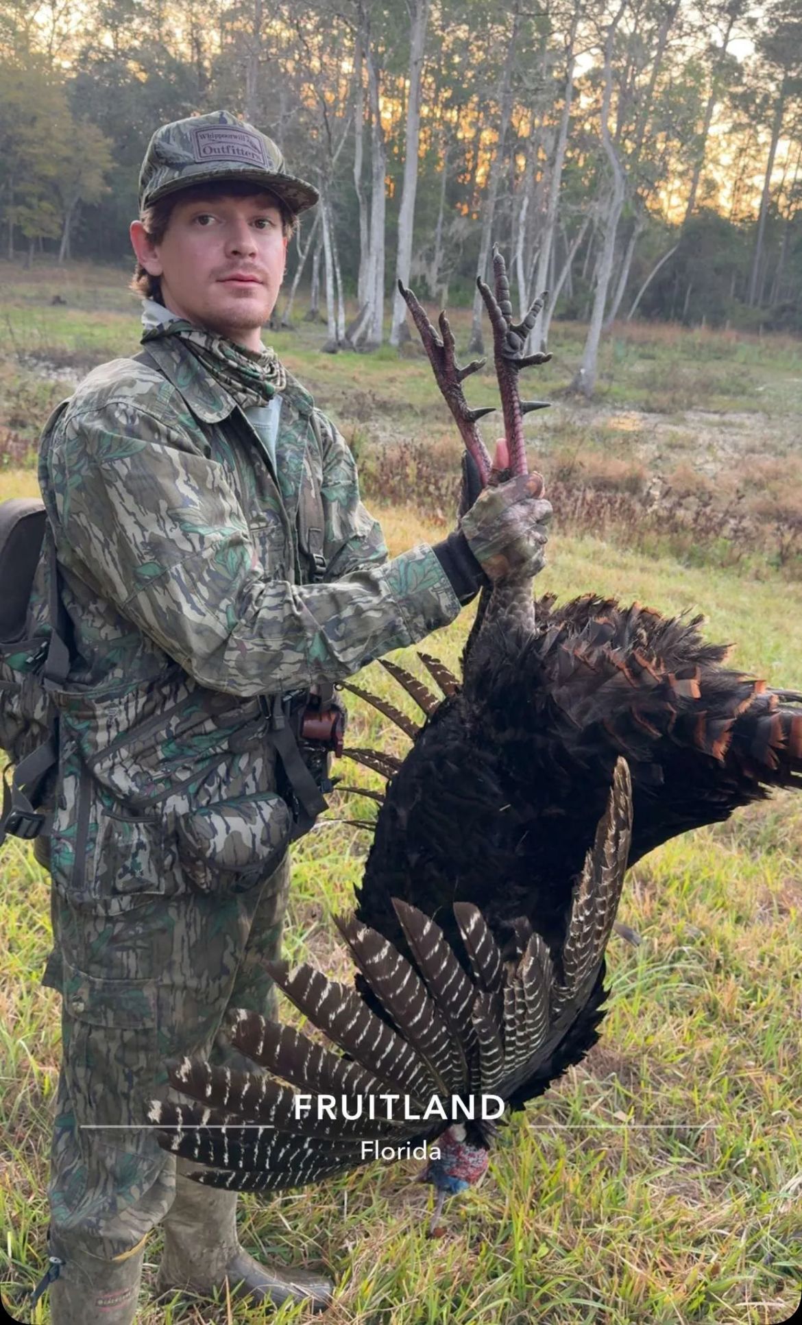 Man in camouflage holds a wild turkey in a wooded setting.