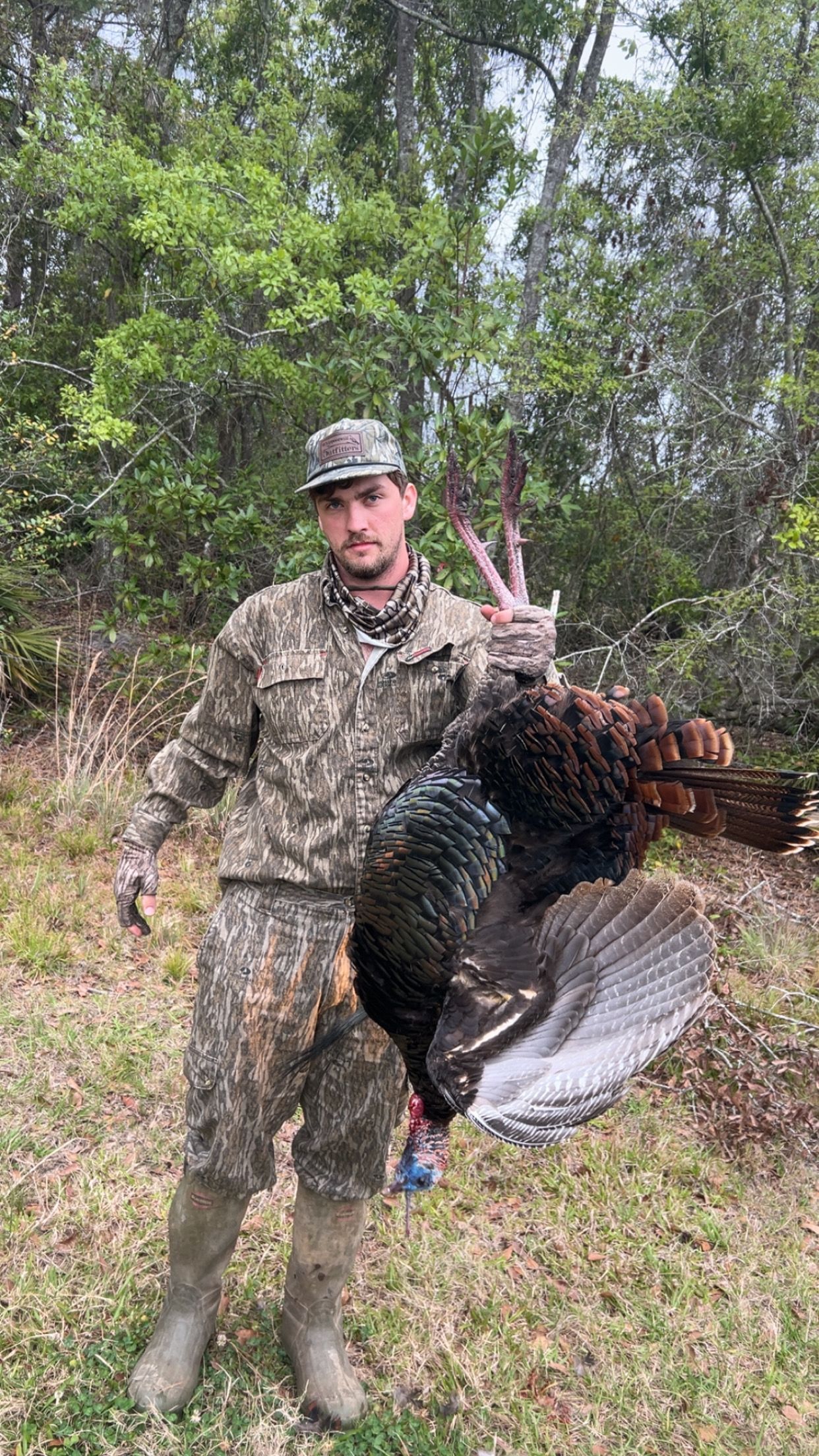 Hunter in camouflage holding a wild turkey in a wooded area.