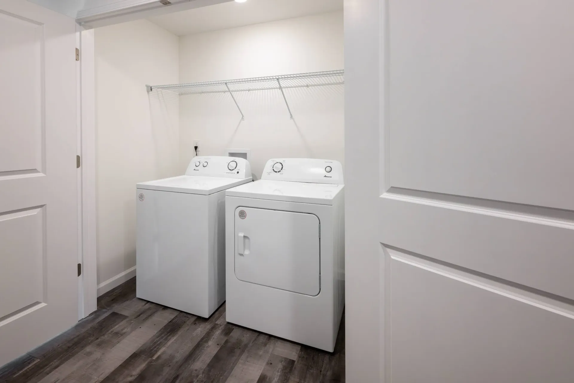 Laundry closet with white washer and dryer side by side under a wire shelf.