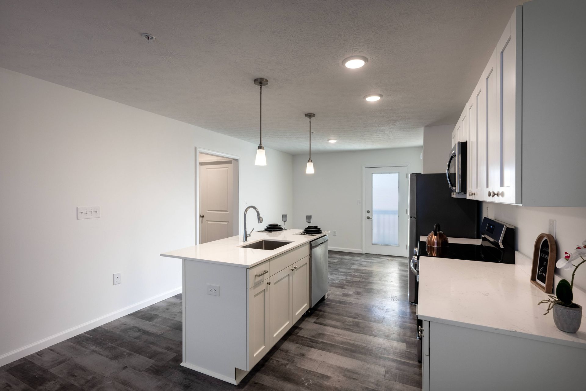 Modern kitchen with white cabinets, island, stainless steel appliances, and dark gray flooring.