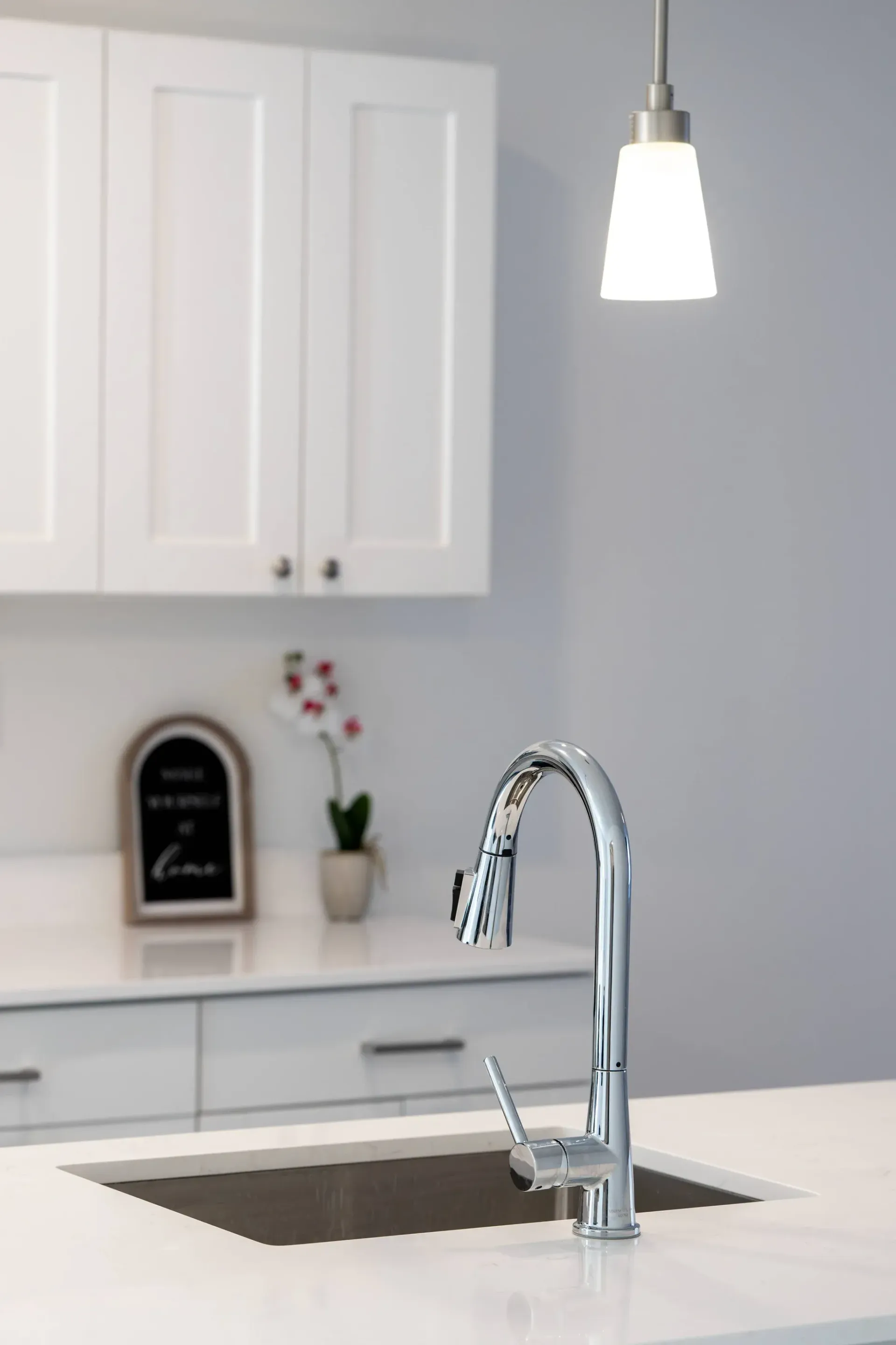 Modern kitchen with chrome gooseneck faucet over an undermount sink, white cabinets, and a pendant light.