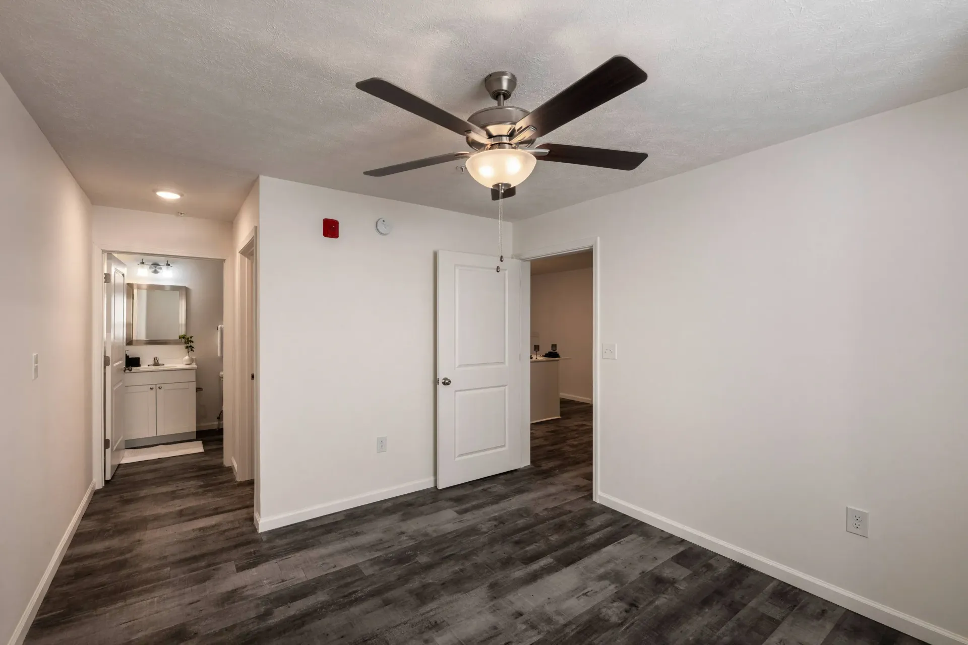 Interior of an apartment living area with a ceiling fan and doorway to a bathroom.