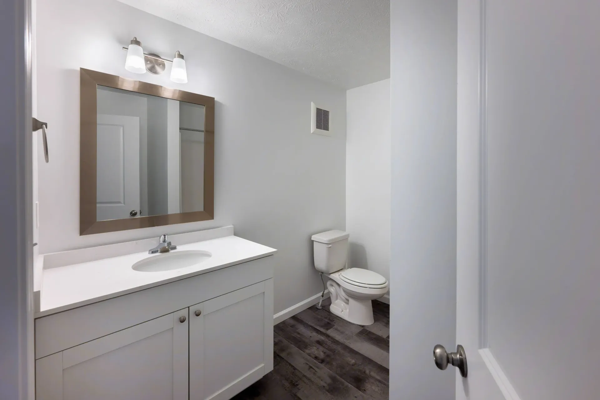 Bathroom with white vanity, framed mirror, two-light fixture, and toilet.