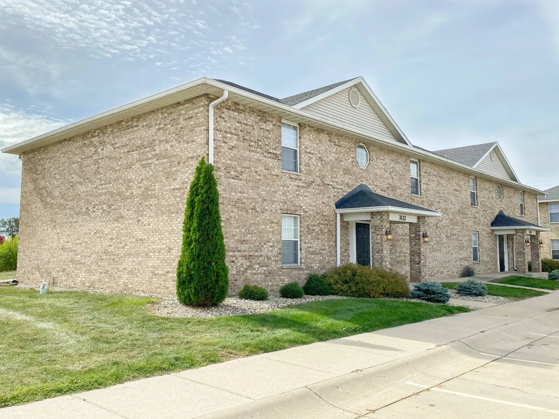 Exterior view of a brick apartment building with multiple entryways and landscaped lawn.