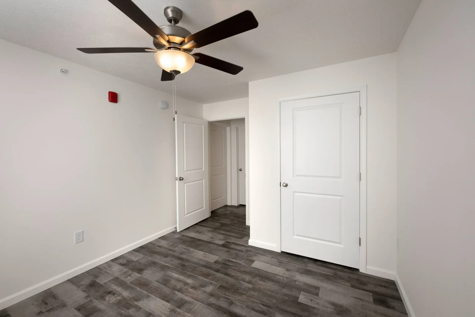Empty bedroom with gray flooring, white walls, two closed doors, and a ceiling fan.