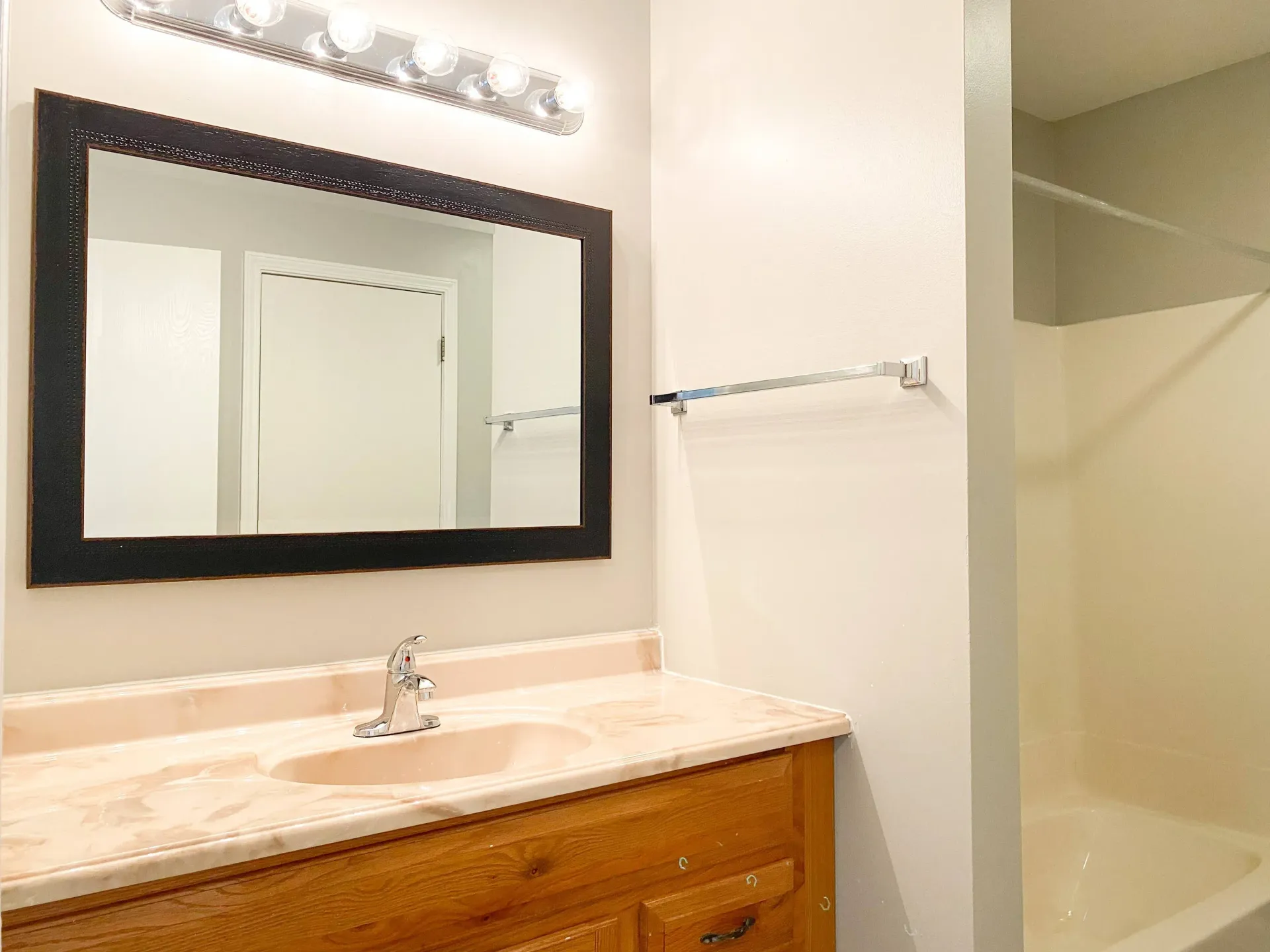 Bathroom vanity with marble countertop, framed mirror, towel bar, and tub/shower.