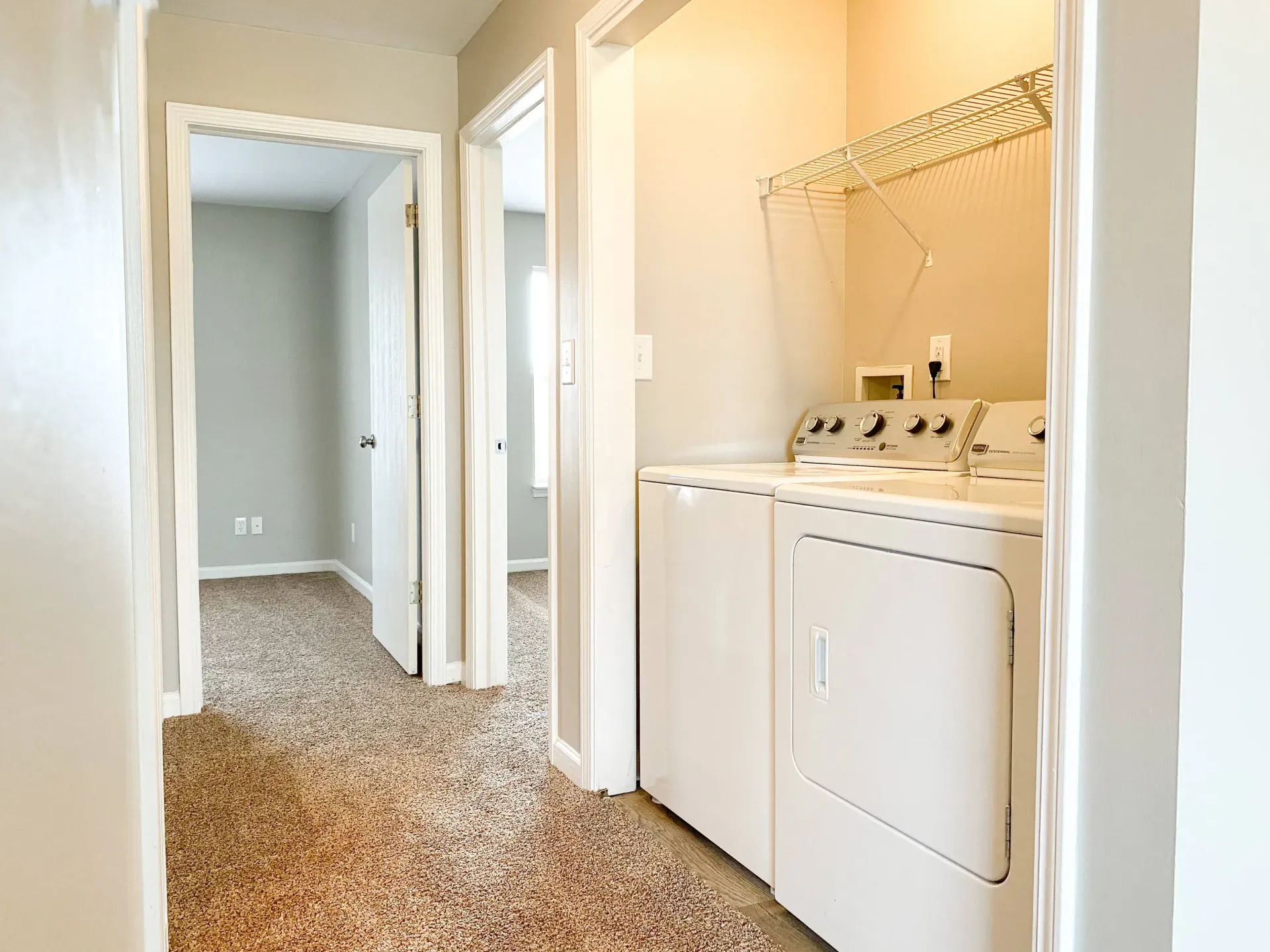 In-unit laundry closet with a side-by-side washer and dryer and a wire shelf above.