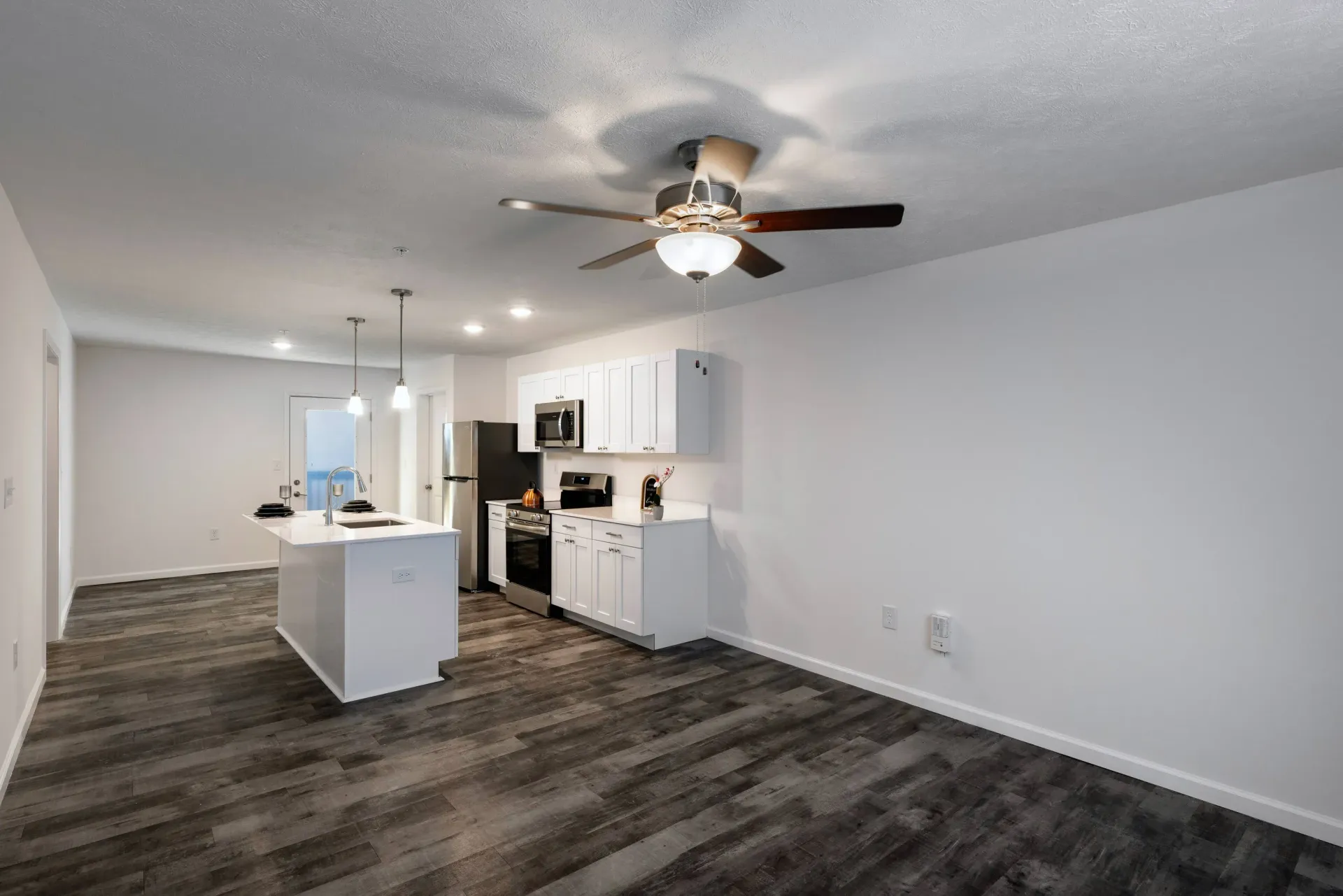 Open-concept kitchen with island, white cabinets, stainless-steel appliances, and a ceiling fan.