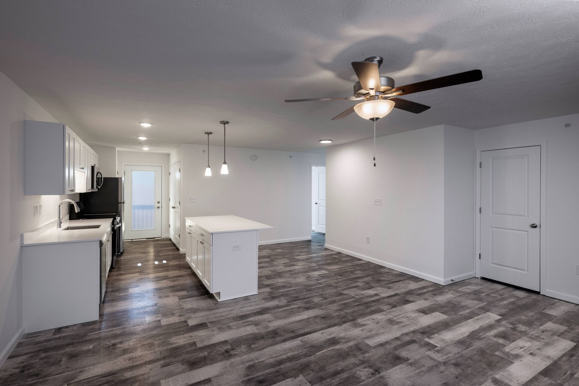 Modern kitchen and living area with white walls, cabinets, island, and dark wood-look flooring.