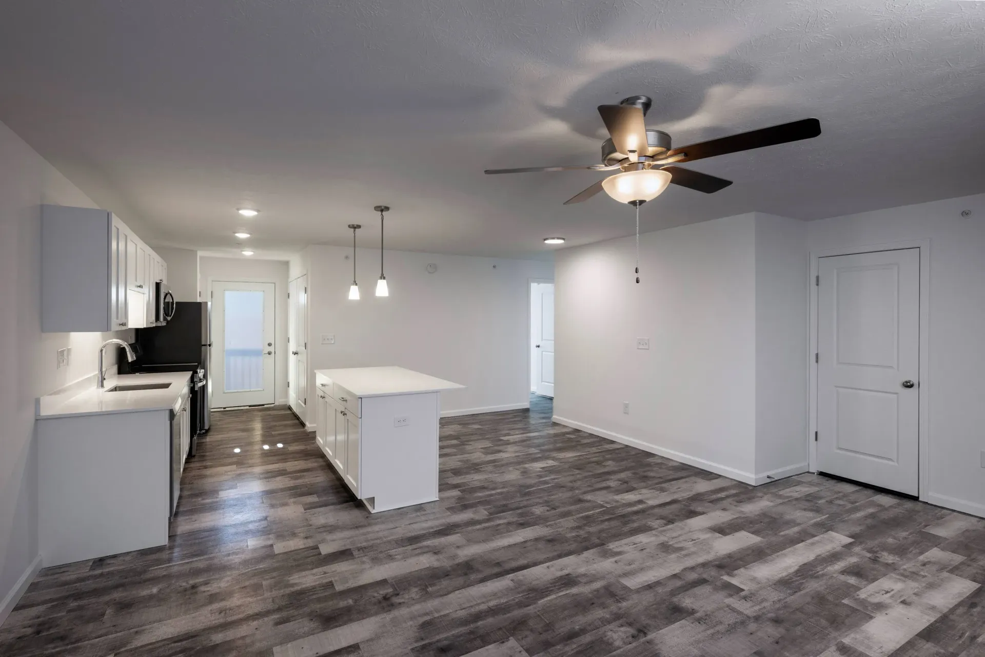 Open-concept kitchen and living area with white cabinets, island, and a ceiling fan.