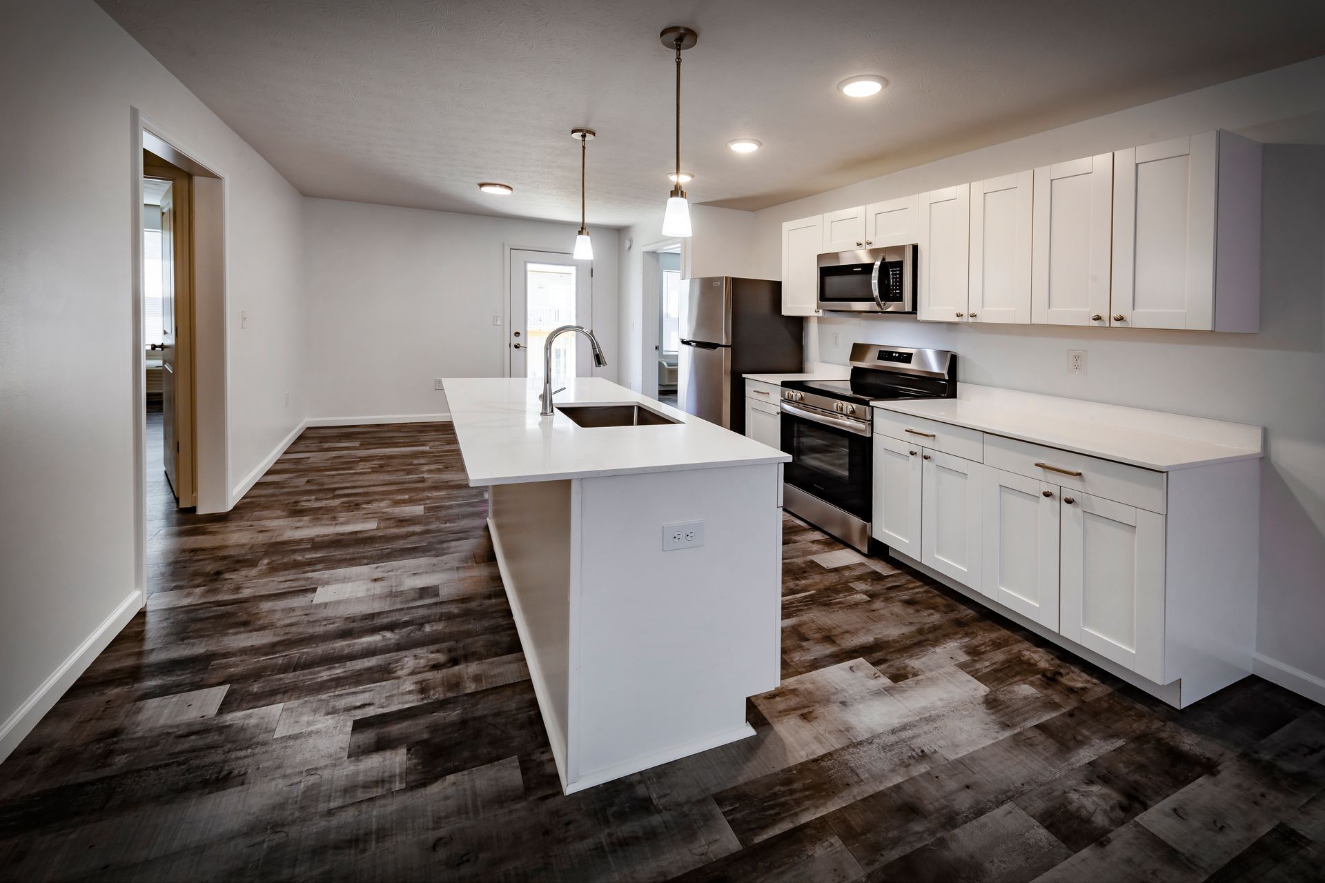 Bright modern kitchen with white cabinets, island, stainless appliances, and dark wood flooring